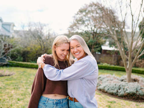Mum hugging teenage daughter while standing in the backyard of their new home on a sunny day - Australian Stock Image
