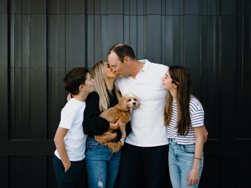 Mum kissing dad on the cheek while their kids are looking at them. - Australian Stock Image