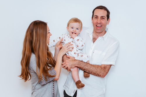 mum plays with young boy with dad holds him up and smile together on white background - Australian Stock Image