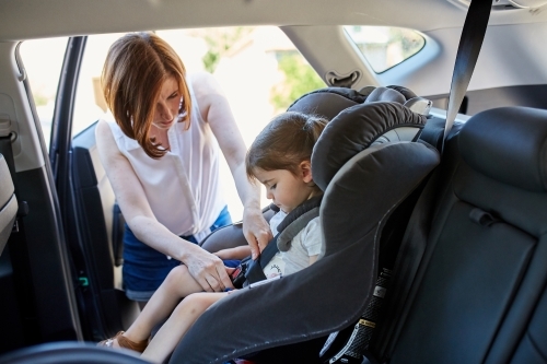 Mum putting daughter in child car seat - Australian Stock Image
