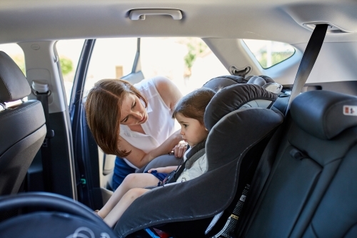 Mum putting daughter in child car seat - Australian Stock Image