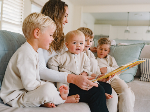 Mum reading a book to her sons seated on the couch - Australian Stock Image