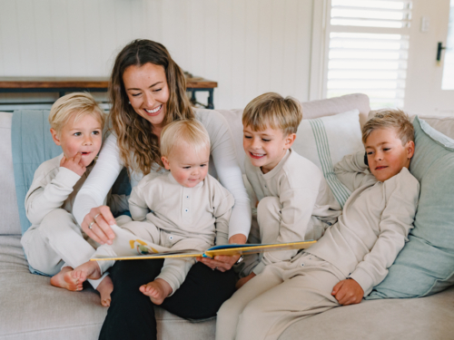 Mum reading a book to her sons seated on the couch - Australian Stock Image