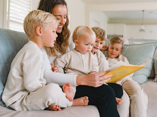 Mum reading a book to her sons seated on the couch - Australian Stock Image