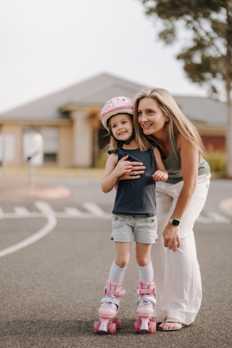 Mum together with daughter on roller blades on the street. - Australian Stock Image