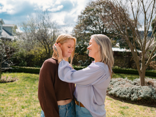 Mum tucking teenage daughters hair behind her ear in the backyard on sunny day - Australian Stock Image