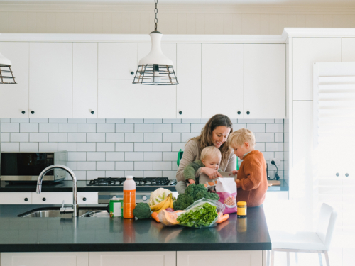 mum with young boys sitting on the kitchen counter by fresh fruits and vegetables from the shops - Australian Stock Image