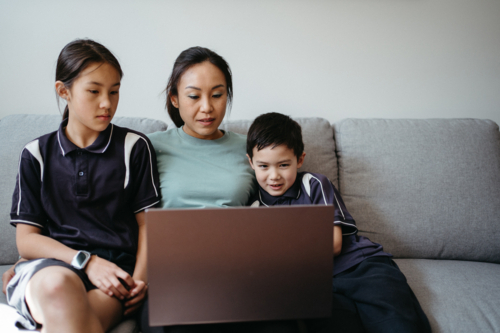 Mum working on her laptop while sitting on the couch with her children. - Australian Stock Image