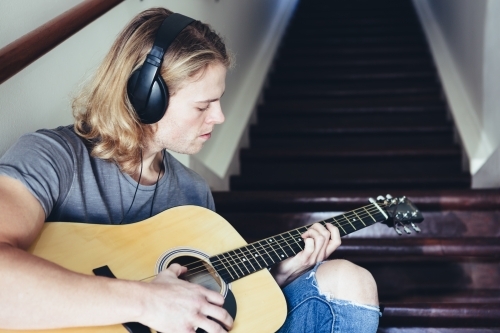 Musician playing guitar with headphones on - Australian Stock Image