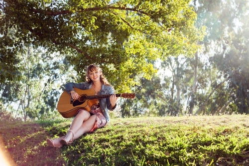 Musician sitting on a hill outside playing guitar - Australian Stock Image