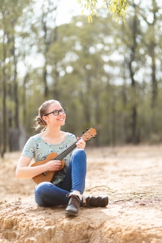 Musician with ukulele playing instrument in dry paddock - Australian Stock Image