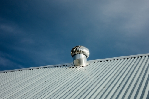 New stainless steel air ventilator on the metal roof against blue sky.