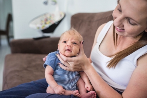 Newborn baby being held sitting on mothers lap smiling - Australian Stock Image