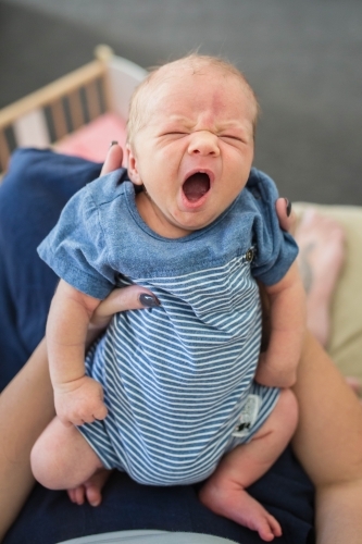 Newborn baby boy lying in mother's arms yawning - Australian Stock Image