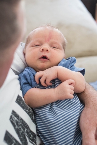 Newborn baby boy lying sleepily in father's arms - Australian Stock Image