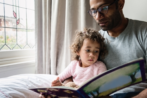 Father reading daughter a story book - Australian Stock Image
