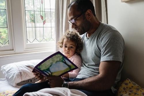 Father reading daughter a story book - Australian Stock Image