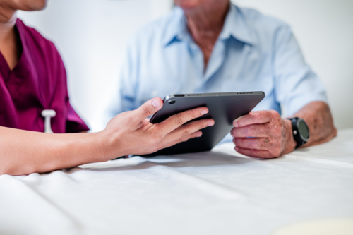 Nurse shows health information to an elderly man on a tablet at a healthcare setting - Australian Stock Image