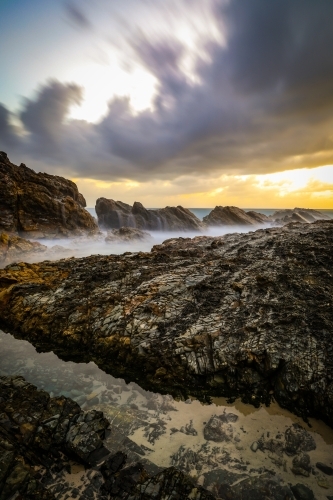 Ocean and rocky coastline against cloudy sunrise - Australian Stock Image