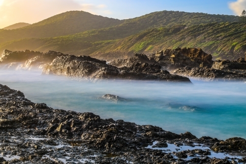 Ocean and rocky coastline against cloudy sunrise - Australian Stock Image