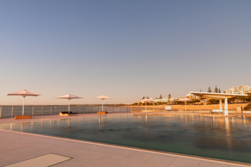 Ocean pool with 4 white umbrellas at sunrise - Australian Stock Image