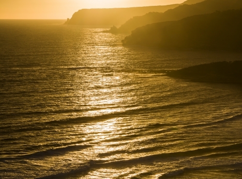 Ocean waves, headlands and sea mist in golden sunset light