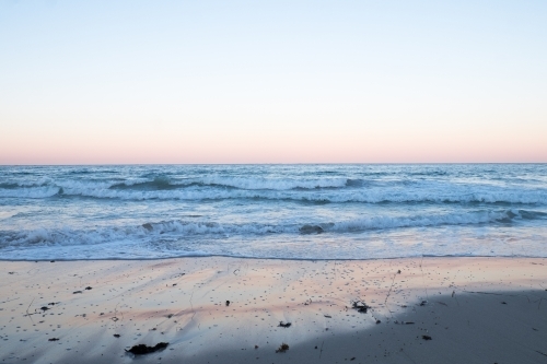 Ocean waves lapping and light reflections in the sand in the morning pastel pink light - Australian Stock Image