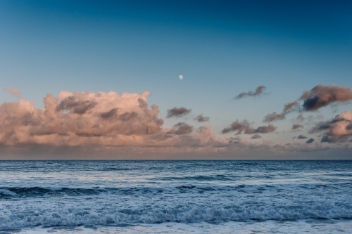 Ocean with pink clouds and moon - Australian Stock Image