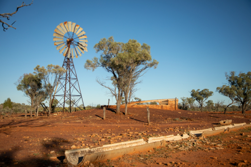 Old abandoned windmill and turkey nest with trough in the foreground - Australian Stock Image
