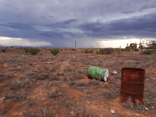 old barrels in barren landscape with storm in background - Australian Stock Image