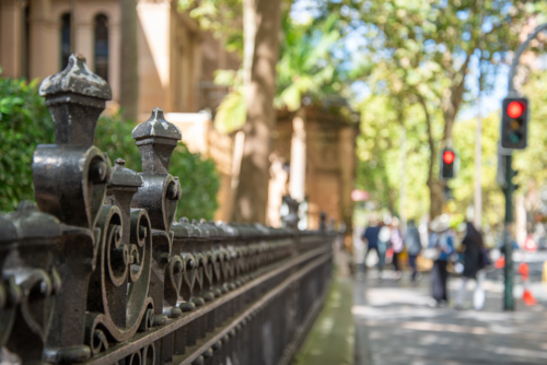 Old cast iron fence with pedestrians and traffic lights out of focus in the background - Australian Stock Image