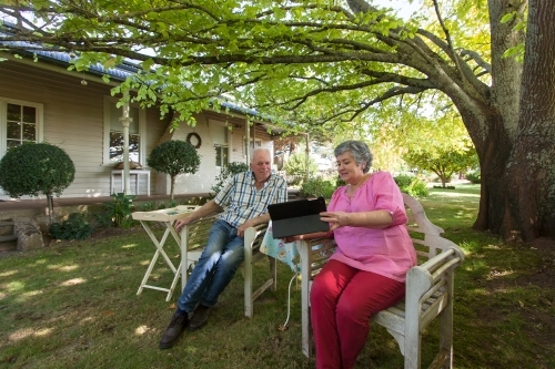 Old couple sitting on the bench looking at their tablet - Australian Stock Image