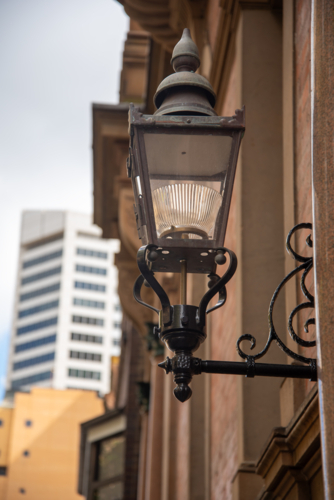 Old light on a sandstone building with modern buildings in the background - Australian Stock Image