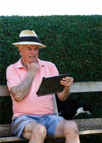 Old man sitting on a bench looking at his tablet