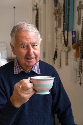 Old man with a cup of tea looks at the camera