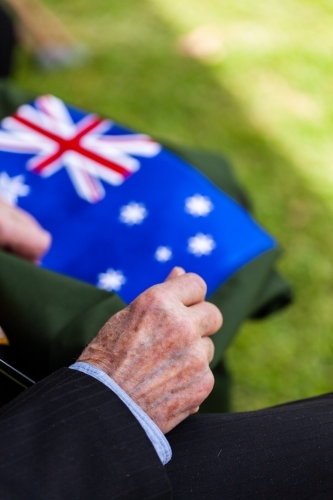 old mans hands resting beside australian flag at remembrance day ceremony - Australian Stock Image