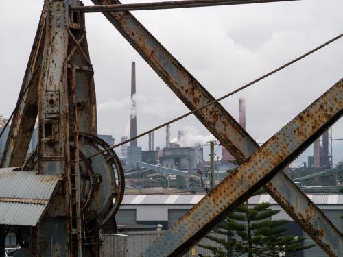 Old steam crane with steelworks in the background on overcast day - Australian Stock Image