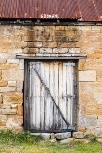 Old timber door on stone brick building with rusted corrugated roof. - Australian Stock Image