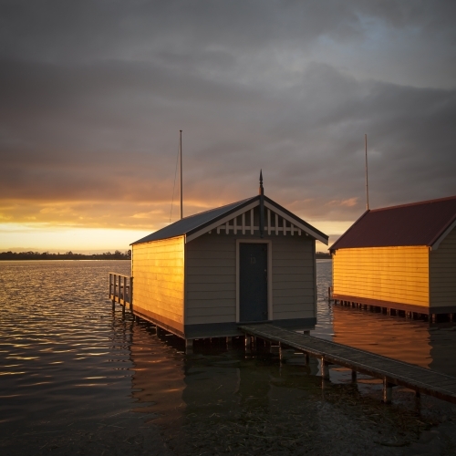 Old weathered boat sheds on lake at sunset - Australian Stock Image