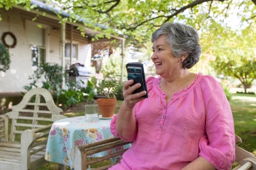 Old woman sitting in backyard looking at her mobile phone