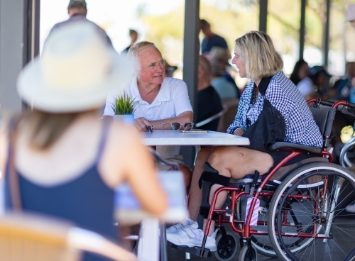 older couple in cafe with woman in wheelchair and blurred person in foreground - Australian Stock Image
