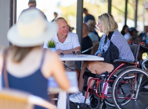 older couple in cafe with woman in wheelchair and blurred person in foreground