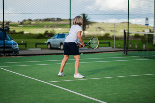 Older female athlete prepares to hit the tennis ball on green court - Australian Stock Image