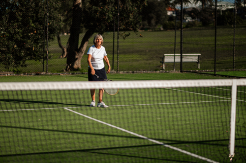 Older female athlete prepares to serve on tennis court - Australian Stock Image