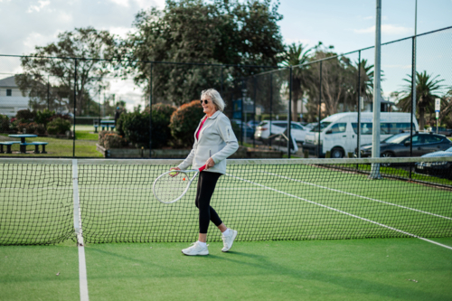 Older female athlete walks on a tennis court, enjoying an afternoon match. - Australian Stock Image