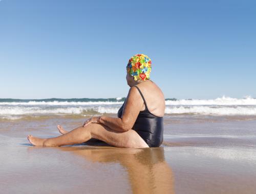 Older lady in swimmers sitting on the beach - Australian Stock Image
