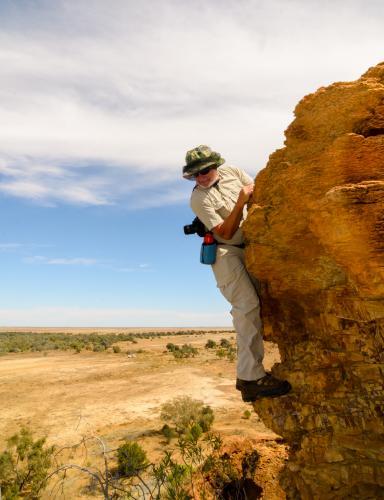 Older man climbing on cliff and looking down - Australian Stock Image