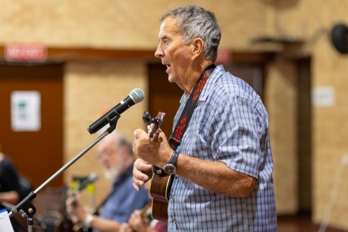 older man playing ukelele and singing into microphone