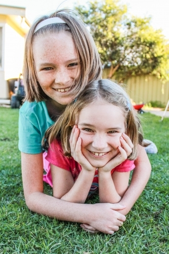 Older sister lying on top of younger sister happy smiling - Australian Stock Image