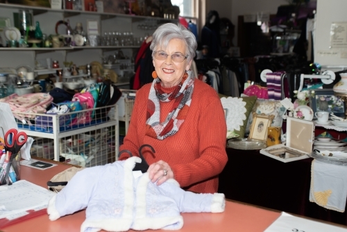Older smiling lady showing baby clothes in an op shop